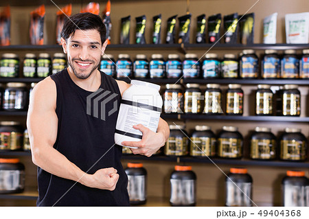 Young bodybuilder showing his biceps and holding pot of sport nutrition products in shop Young bodybuilder showing his biceps and holding pot of sport nutrition products in shop 49404368