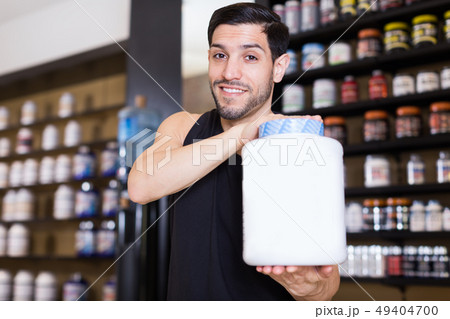Smiling muscular man seller demonstration big pot of sport food 49404700