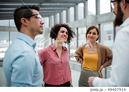 A group of young businesspeople standing in office, talking. 49407914