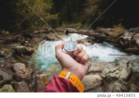A beautiful male hand with a yellow watch strap holds a magnetic compass in a coniferous autumn 49413855