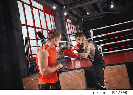 Knockout punch. Strong tattooed athlete in sports clothing training on boxing paws with partner 49422906