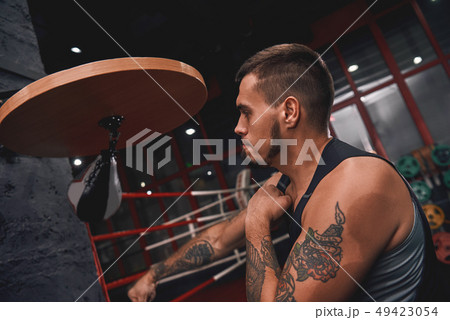 New champion. Close-up of muscular tattooed boxer in sports clothing hitting punching speed bag 49423054
