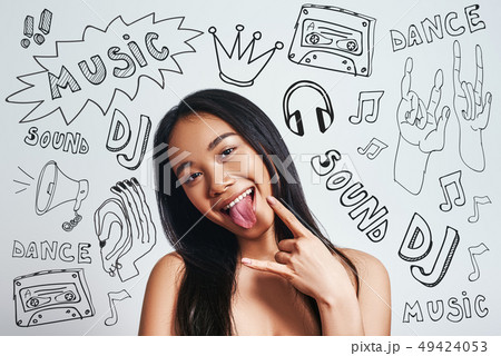 Music is my freedom. Joyful young age asian woman gesturing and sticking out tongue while standing 49424053