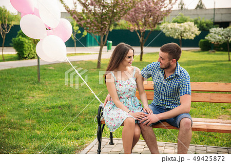 Couple siting on a bench and hold pink helium balls Couple siting on a bench and hold pink helium balls 49425872