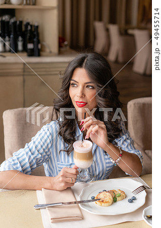 Beautiful young woman enjoying coffee cappuccino or latte in a glass cup with foam. Light breakfast 49455714