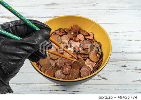 Bowl full of coins of the pound sterling and a hand holding chopsticks.Concept 49455774