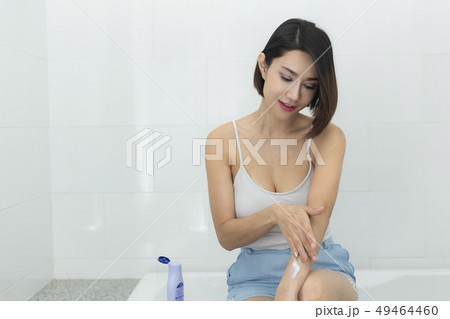 Young woman applying body cream in bathroom. 49464460