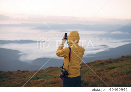 Man in yellow jacket taking photograph on smart phone in the Carpathian Mountain Range Man in yellow jacket taking photograph on smart phone in the Carpathian Mountain Range 49469942