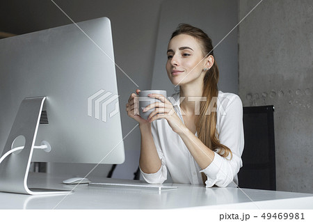 Young businesswoman holding coffee cup at desk Young businesswoman holding coffee cup at desk 49469981
