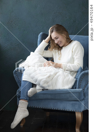 Smiling woman witting in armchair with white blanket Smiling woman witting in armchair with white blanket 49470164