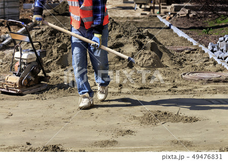 Laying tiles on the sidewalk, a worker carries 49476831