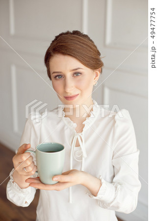 Attractive young woman in casual clothes is holding a cup, looking away and smiling, on white 49477754
