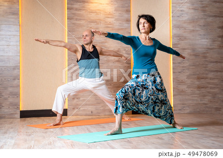 Man and woman with outstretched arms are practicing yoga while standing on blue mat. Man and woman with outstretched arms are practicing yoga while standing on blue mat. 49478069