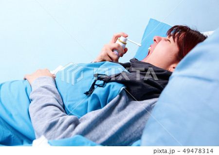 Photo of sick brunette using throat spray lying in bed Photo of sick brunette using throat spray lying in bed 49478314