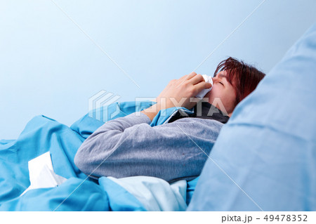 Photo of side of sick brunette blowing her nose in paper handkerchief lying in bed. Photo of side of sick brunette blowing her nose in paper handkerchief lying in bed. 49478352