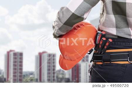 A female construction worker with safety helmet against city background A female construction worker with safety helmet against city background 49500720