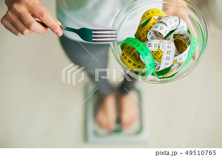 Diet and Weight Loss. Woman holds bowl and fork with measuring tape Diet and Weight Loss. Woman holds bowl and fork with measuring tape 49510765