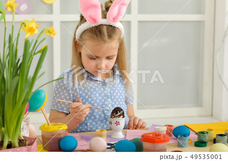 little child girl with Easter bunny ears painting Easter eggs at home. 49535001
