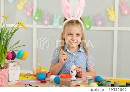 little child girl with Easter bunny ears painting Easter eggs at home. 49535003