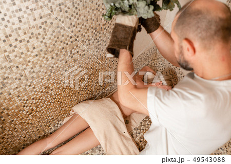 Slim woman in bath is getting steaming massage with hot oak leaves brooms, in steam-room 49543088