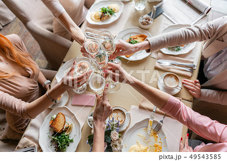 Clink glasses. Five women. Portrait of young people having breakfast at table in restaurant 49543585