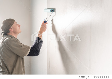 Young man, worker glueing wallpapers on concrete wall. Repair the apartment. Home renovation concept 49544331