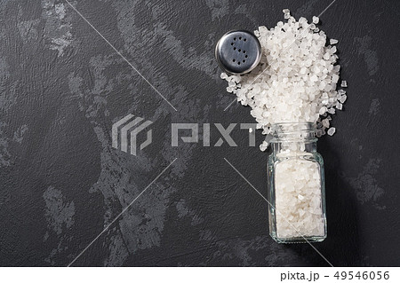 Pile of salt and salt shaker on black stone 49546056