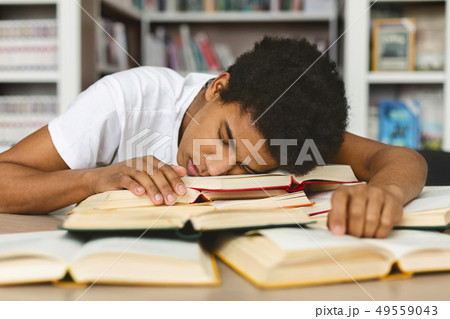 Tired guy napping on books stack in library Tired guy napping on books stack in library 49559043