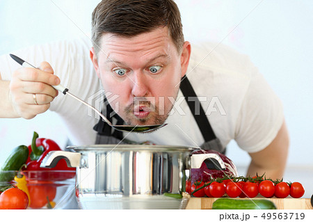 Male cook tries hot soup from pan 49563719