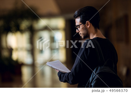 Young student of computer science consults some papers illuminated by the light of a screen in a 49566370