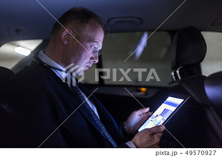 Businessman with a digital tablet sitting in the back seat of a car 49570927
