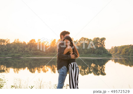 Romantic and people concept - young couple hugging together near the river or lake and enjoying 49572529