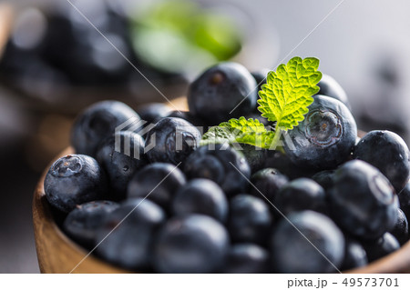 Wooden bowl full of fresh blueberries with herbs 49573701