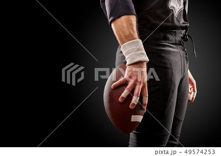 Mid section of American football player with ball against black, copy space, side view 49574253