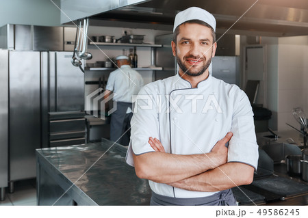We sell flavors. Smiling attractive chef cook with beard standing with hands folded on the kitchen We sell flavors. Smiling attractive chef cook with beard standing with hands folded on the kitchen 49586245