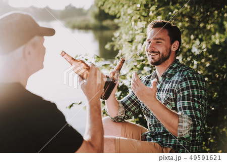 Smiling Men Drinking Beer near River in Summer. Smiling Men Drinking Beer near River in Summer. 49591621
