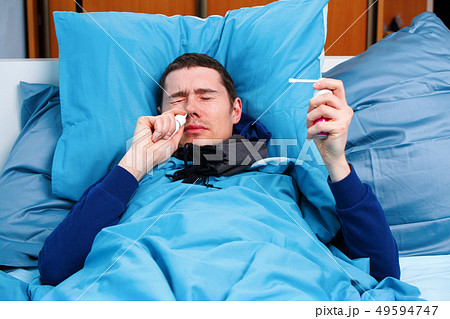 Photo of sick brunet man in scarf with handkerchief and spray with medicine lying in bed . 49594747