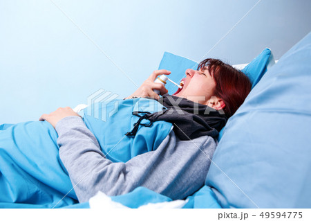 Image of sick brunette using throat spray lying in bed . 49594775