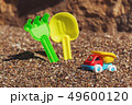 Children's toy truck with gravel or sand. Yellow scoop and green rake on the background. Concept of 49600120