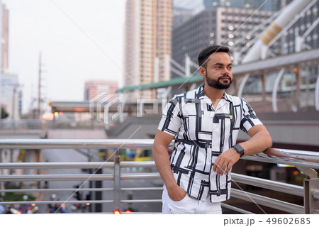 Young bearded Indian man thinking against view of the city outdoors Young bearded Indian man thinking against view of the city outdoors 49602685