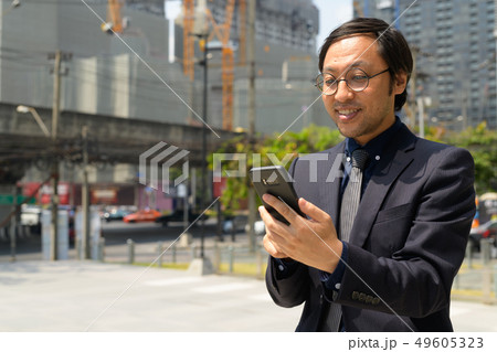 Happy Asian businessman using phone in the city streets outdoors Happy Asian businessman using phone in the city streets outdoors 49605323
