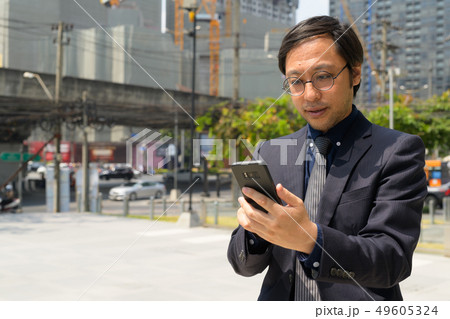 Asian businessman using phone in the city streets outdoors Asian businessman using phone in the city streets outdoors 49605324