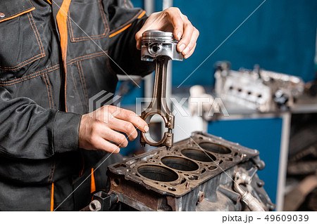 Car mechanic holding a new piston for the engine, overhaul.. Engine on a repair stand with piston 49609039