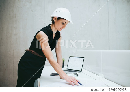 Young businesswoman or architect with helmet and laptop standing in office. 49609293
