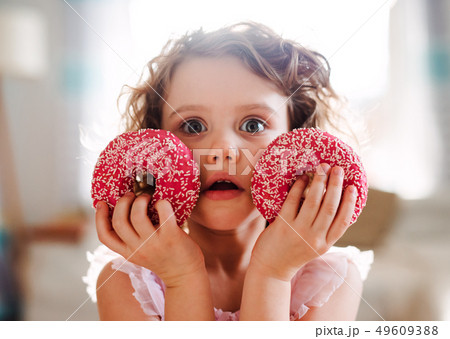 A small girl with doughnuts at home, looking at camera. 49609388