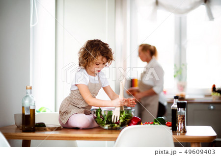 A portrait of small girl with grandmother at home, preparing vegetable salad. A portrait of small girl with grandmother at home, preparing vegetable salad. 49609403