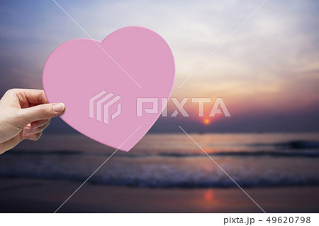 Woman hand holding pink paper heart on the beach 49620798