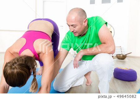 Yoga instructor corrects student's pose 49645082