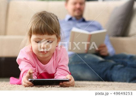 Father and daughter lie on floor using mobile phone 49649253