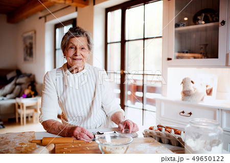 Elderly woman making cakes in a kitchen at home. Copy space. 49650122